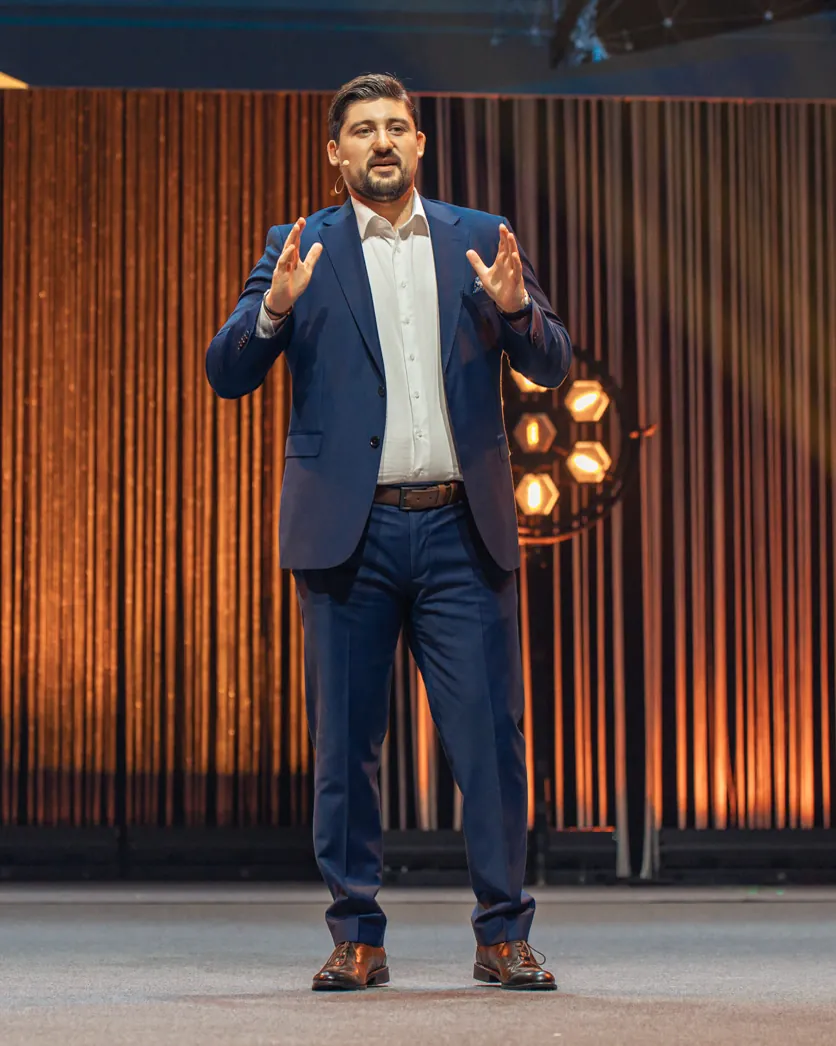 Dr. Radovan Vitosevic explaining on stage in front of an orange curtain
